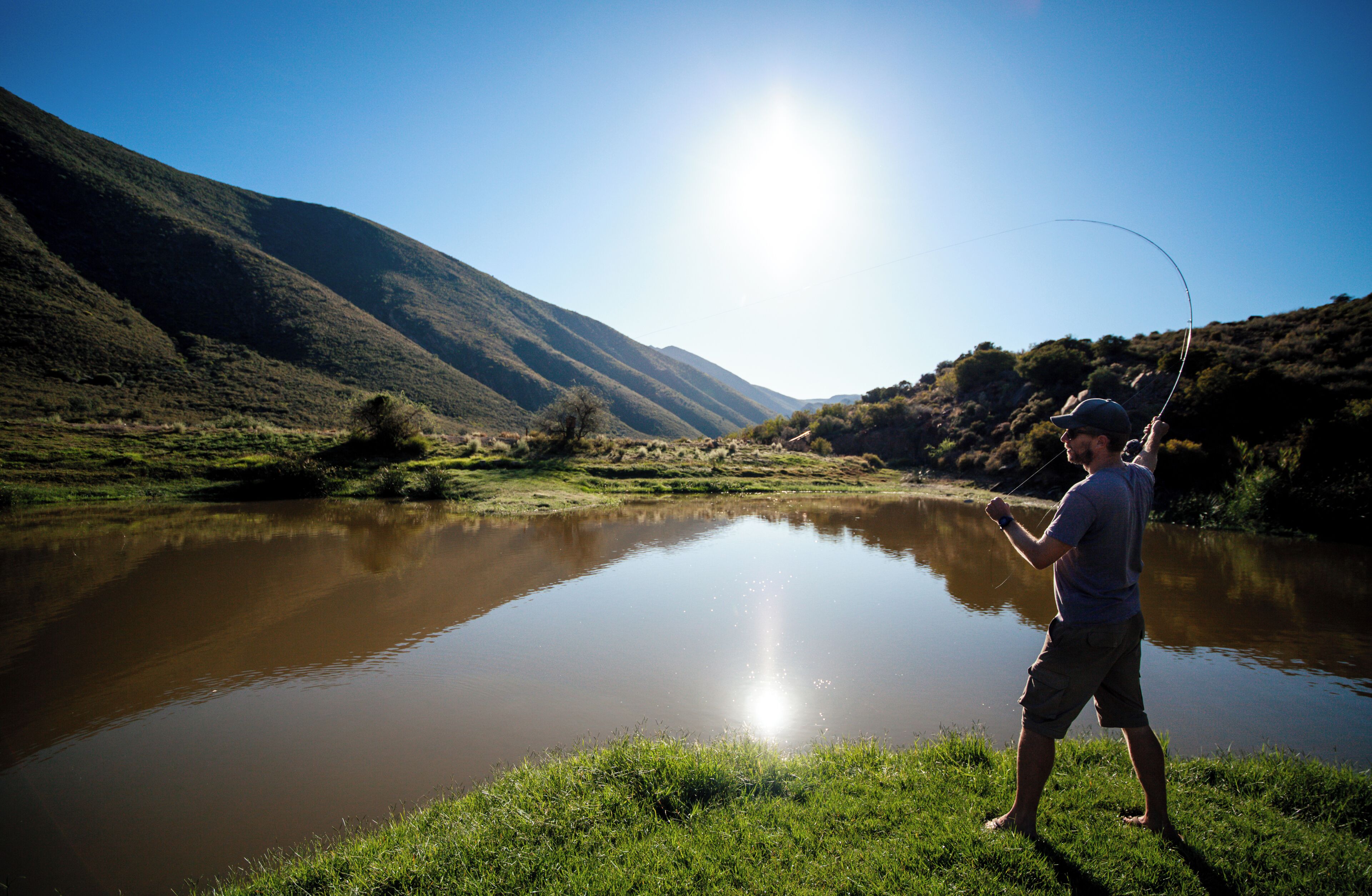 Una persona pescando en un río tranquilo con colinas al fondo.