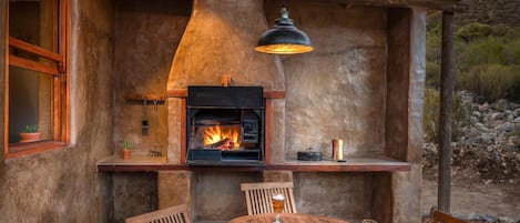 An outdoor patio with a wood-burning stove, a table with chairs, and a glass of beer.