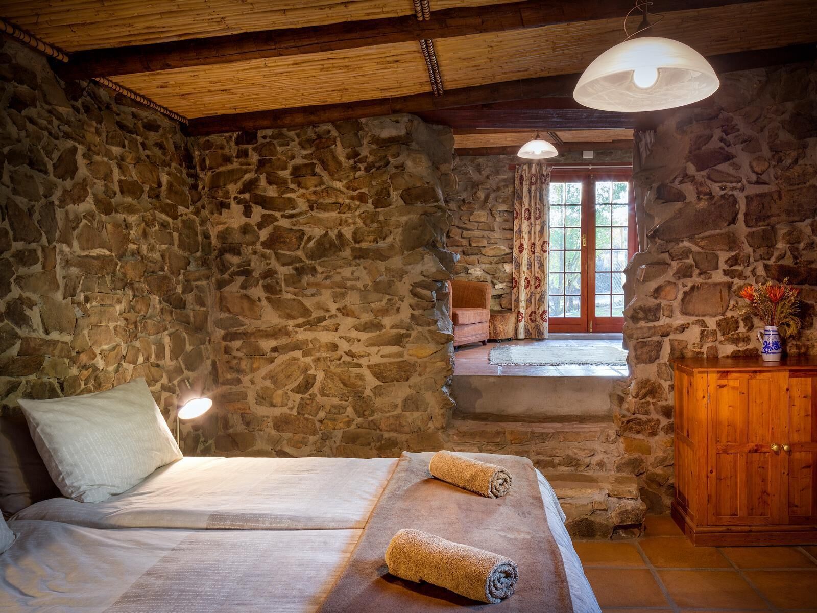 Una habitación con paredes de piedra, una cama, un banco de madera y un armario.