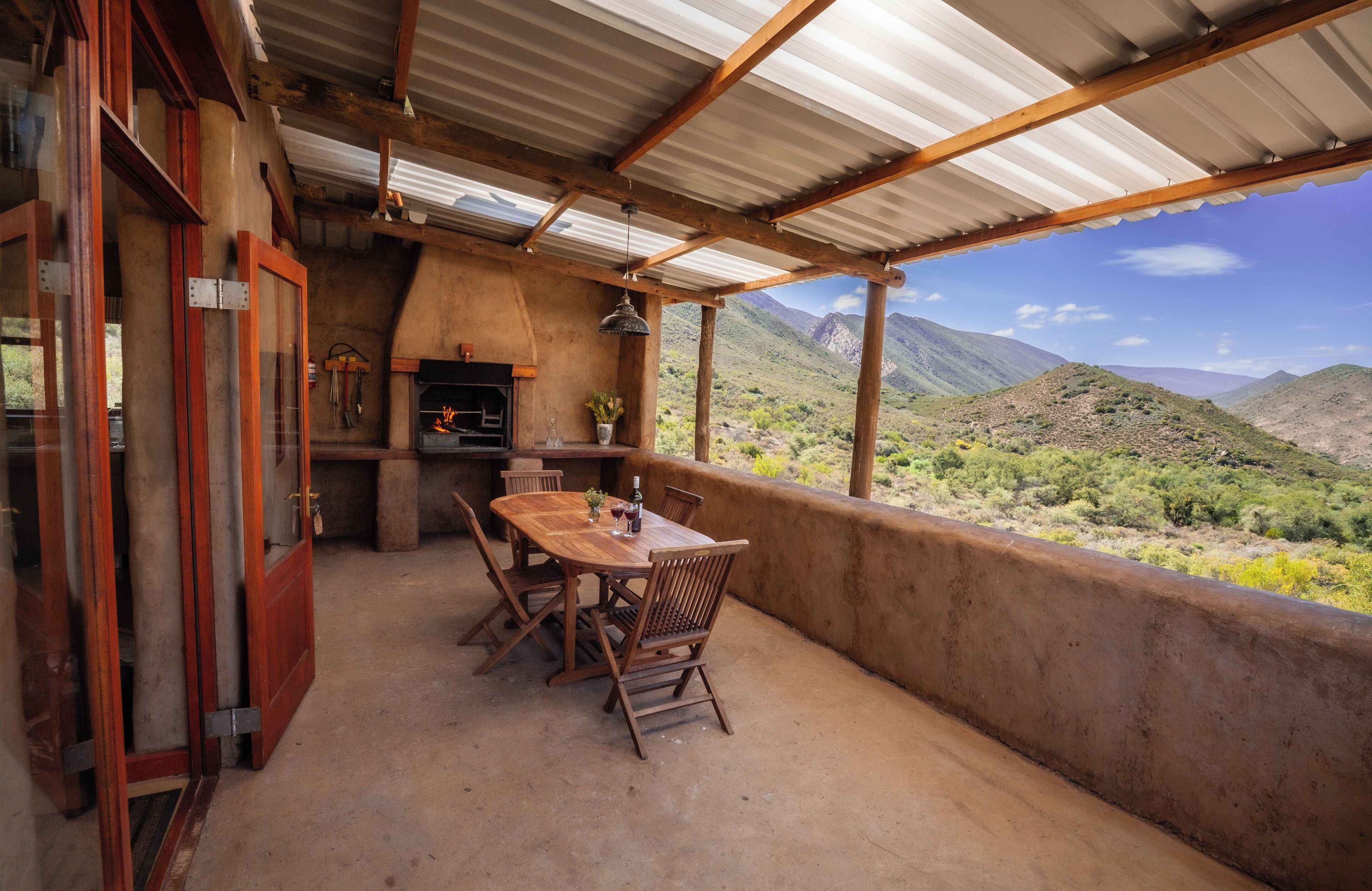 A covered outdoor patio with a wooden table and chairs, a fireplace, and a view of a mountainous landscape.