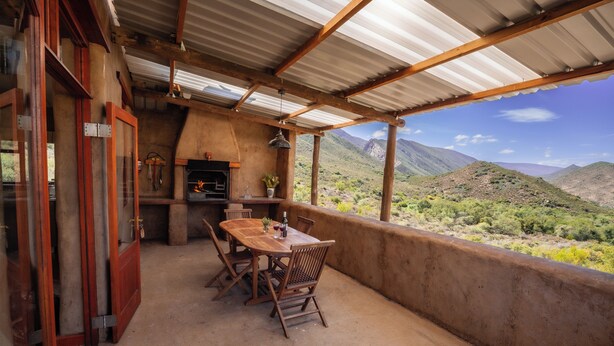 A covered outdoor patio with a wooden table and chairs, a fireplace, and a view of a mountainous landscape.