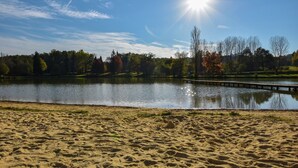 A sandy beach with a calm lake, a wooden pier, and trees in the background. - Holiday Home in Montcléra with Barbecue (Montclera)