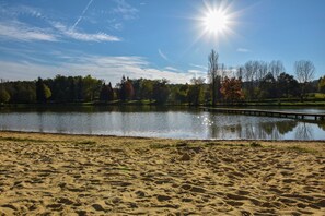Ein Sandstrand mit einem ruhigen See, einer Holzstege und Bäumen im Hintergrund.