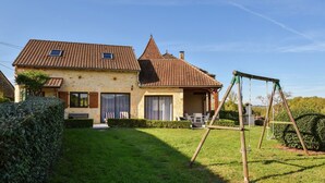 A two-story house with a tiled roof, a swing set, and a well-maintained lawn. - Holiday Home in Montcléra with Barbecue (Montclera)