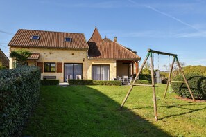 Ein zweistöckiges Haus mit einem Ziegeldach, einer Schaukel und einem gepflegten Rasen.