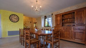 A dining area with a wooden table and chairs, a chandelier, and a clock on the wall. - Holiday Home in Montcléra with Barbecue (Montclera)