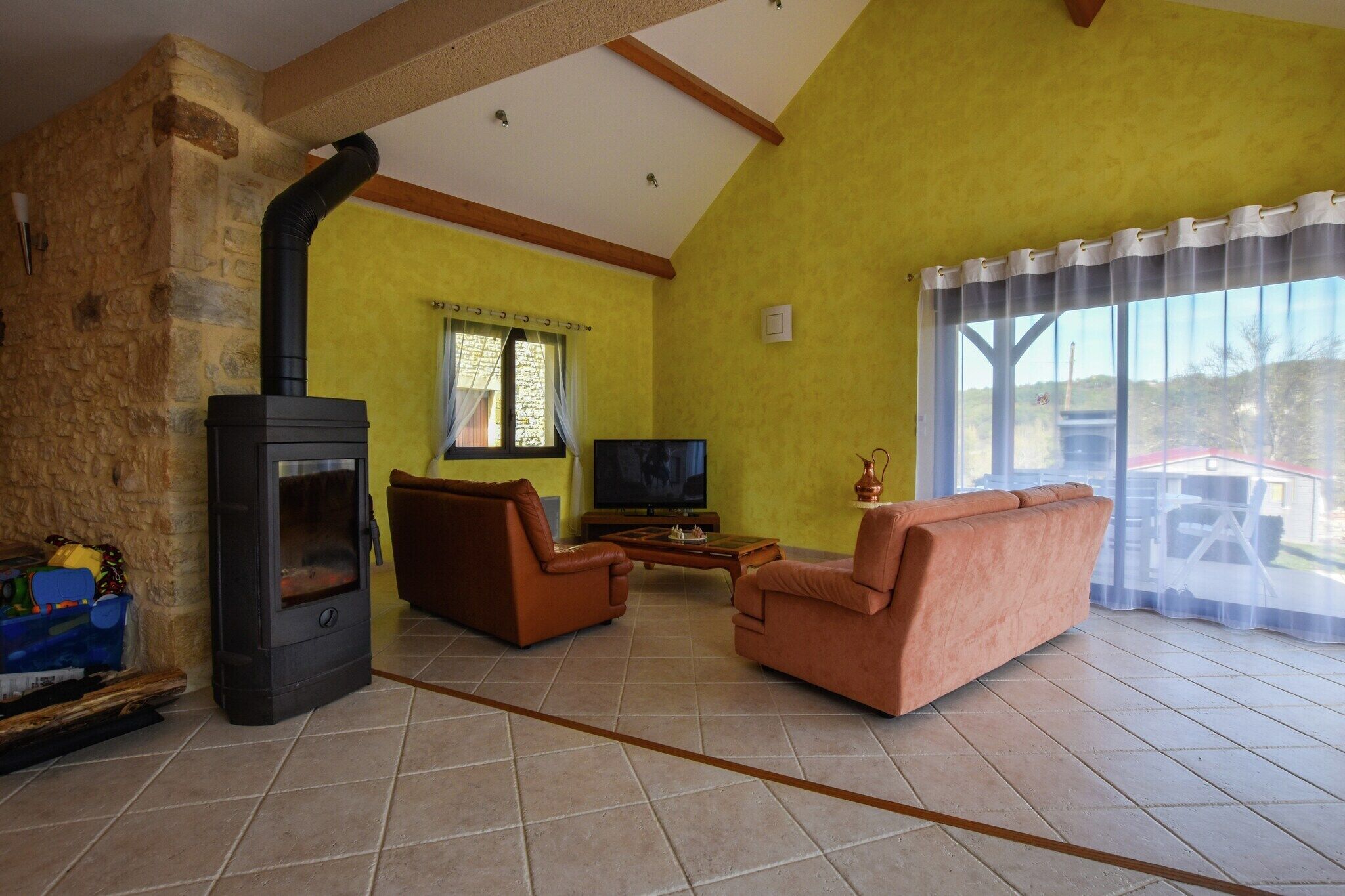 A living room with a stone wall, a fireplace, two sofas, a TV, and a large window with curtains.