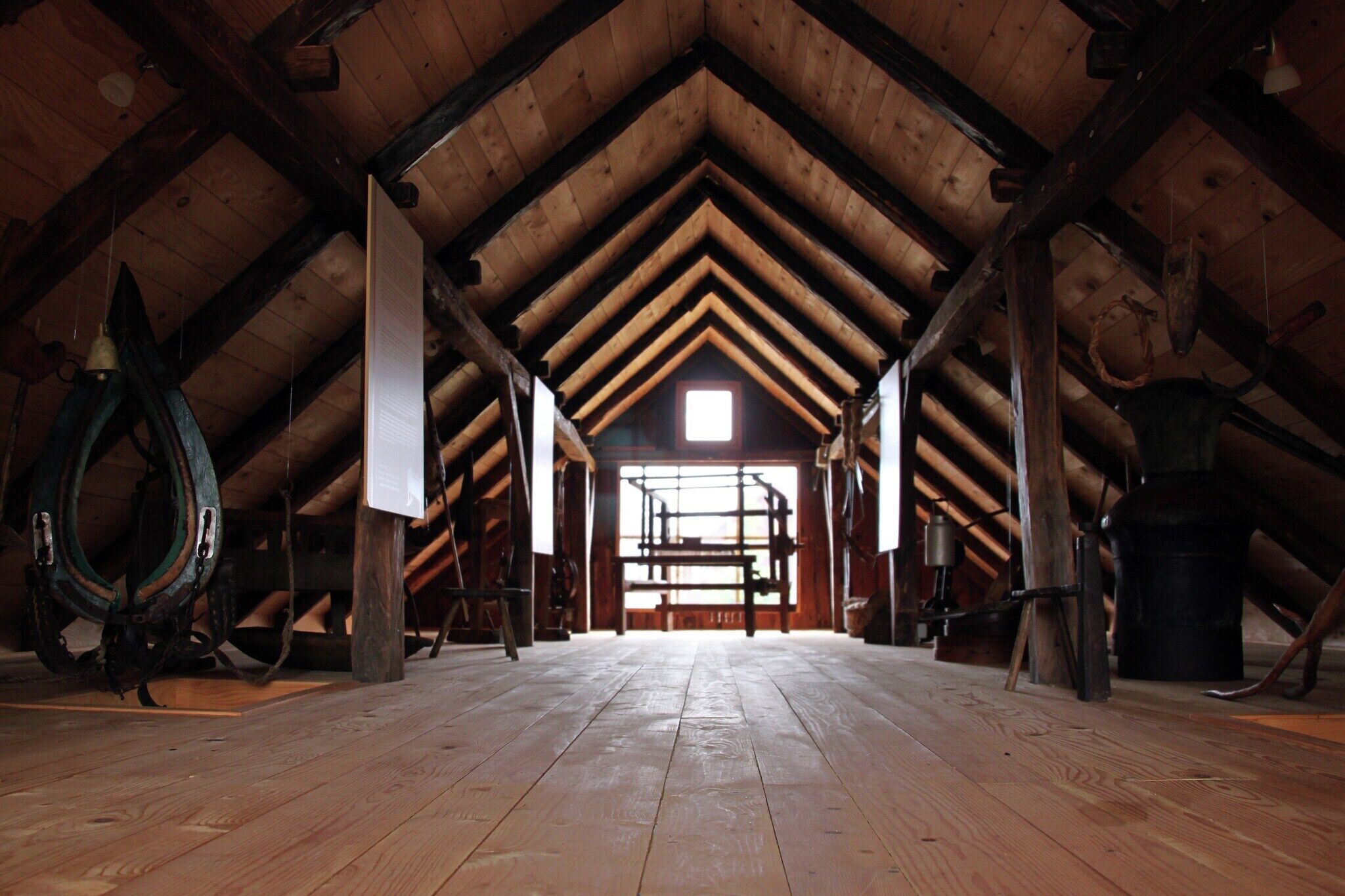 Un espace mansardé avec des poutres en bois, un plancher en bois et une fenêtre au fond.