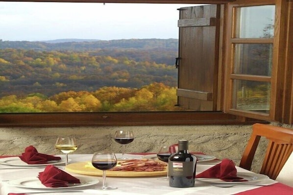 A table set for two with wine glasses, a bottle, and plates, overlooking a forested landscape. - 3BR Country House with Pool & WiFi (Ribnik)