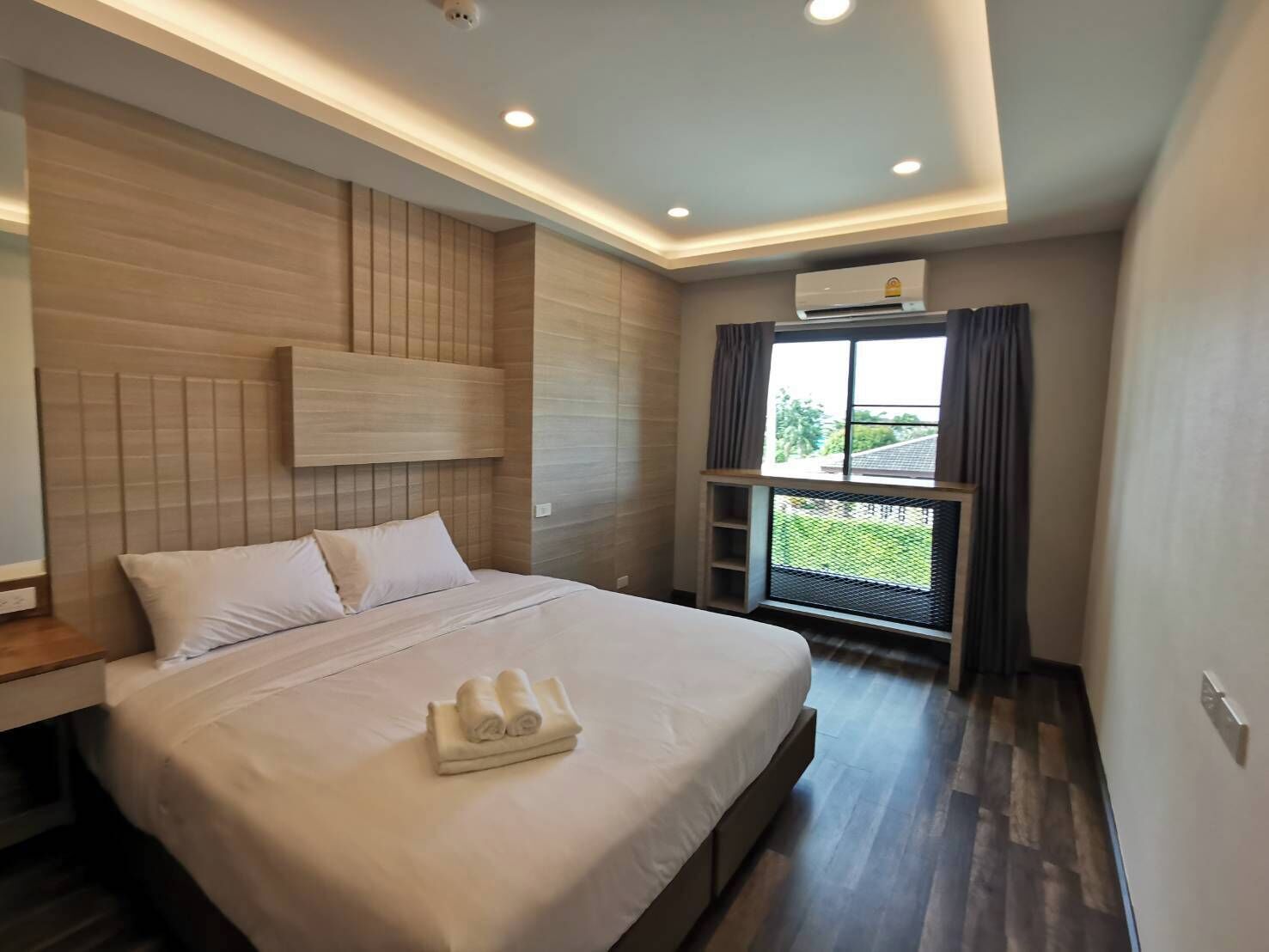 Una habitación de hotel moderna con una cama grande, un cabecero, una ventana con vistas y un equipo de aire acondicionado.