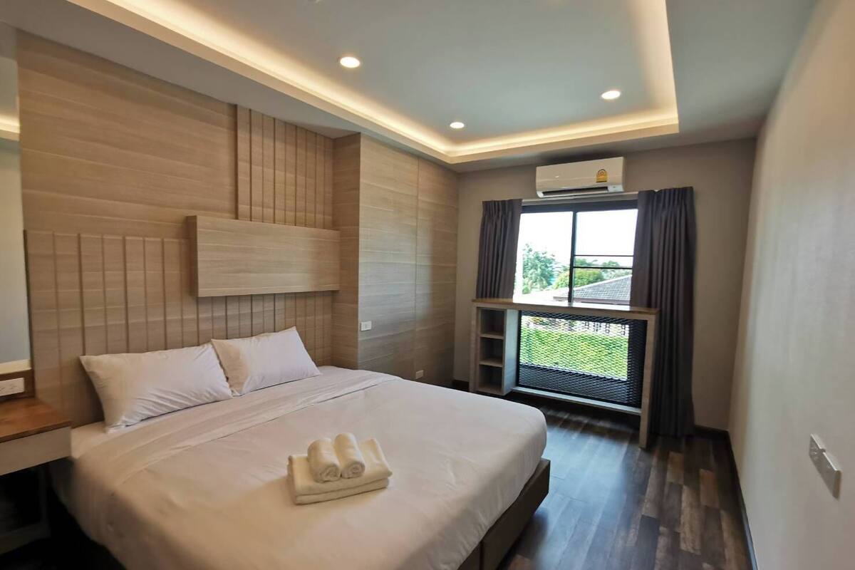 Una habitación de hotel moderna con una cama grande, un cabecero, una ventana con vistas y un equipo de aire acondicionado.