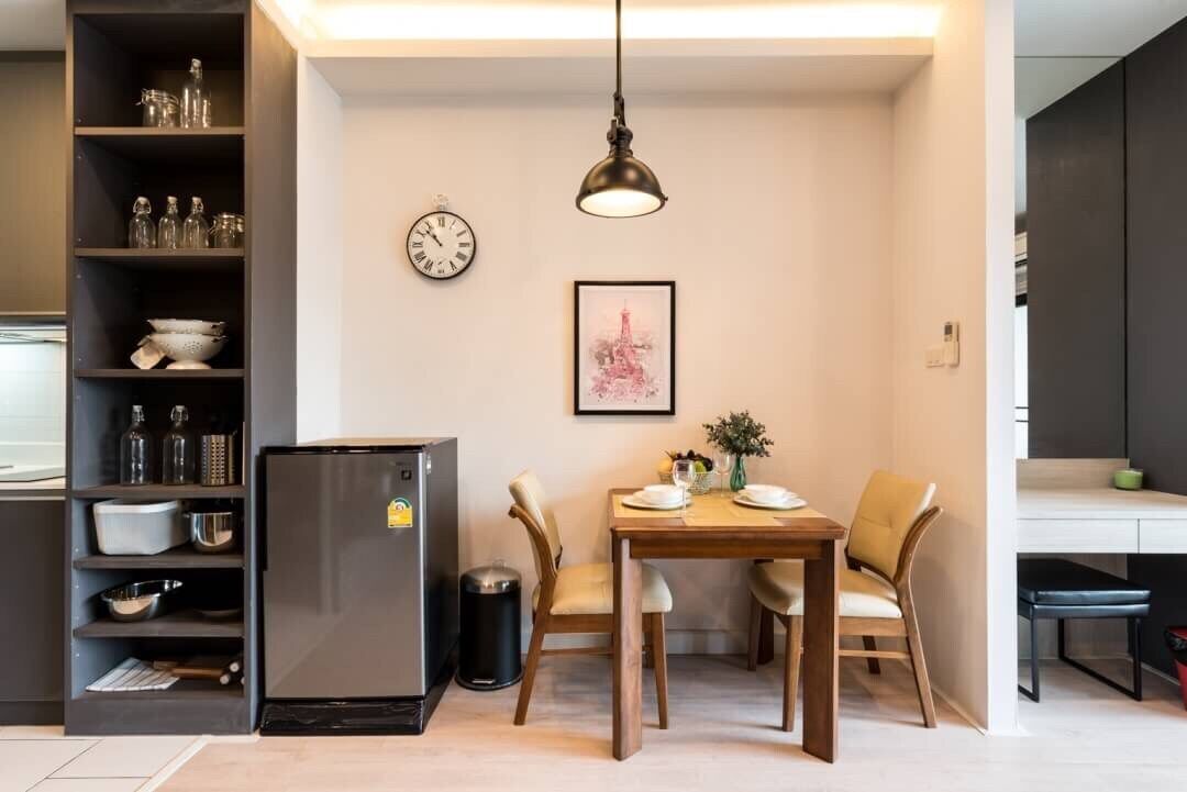 A compact kitchen with a refrigerator, a clock, and a dining table with chairs.