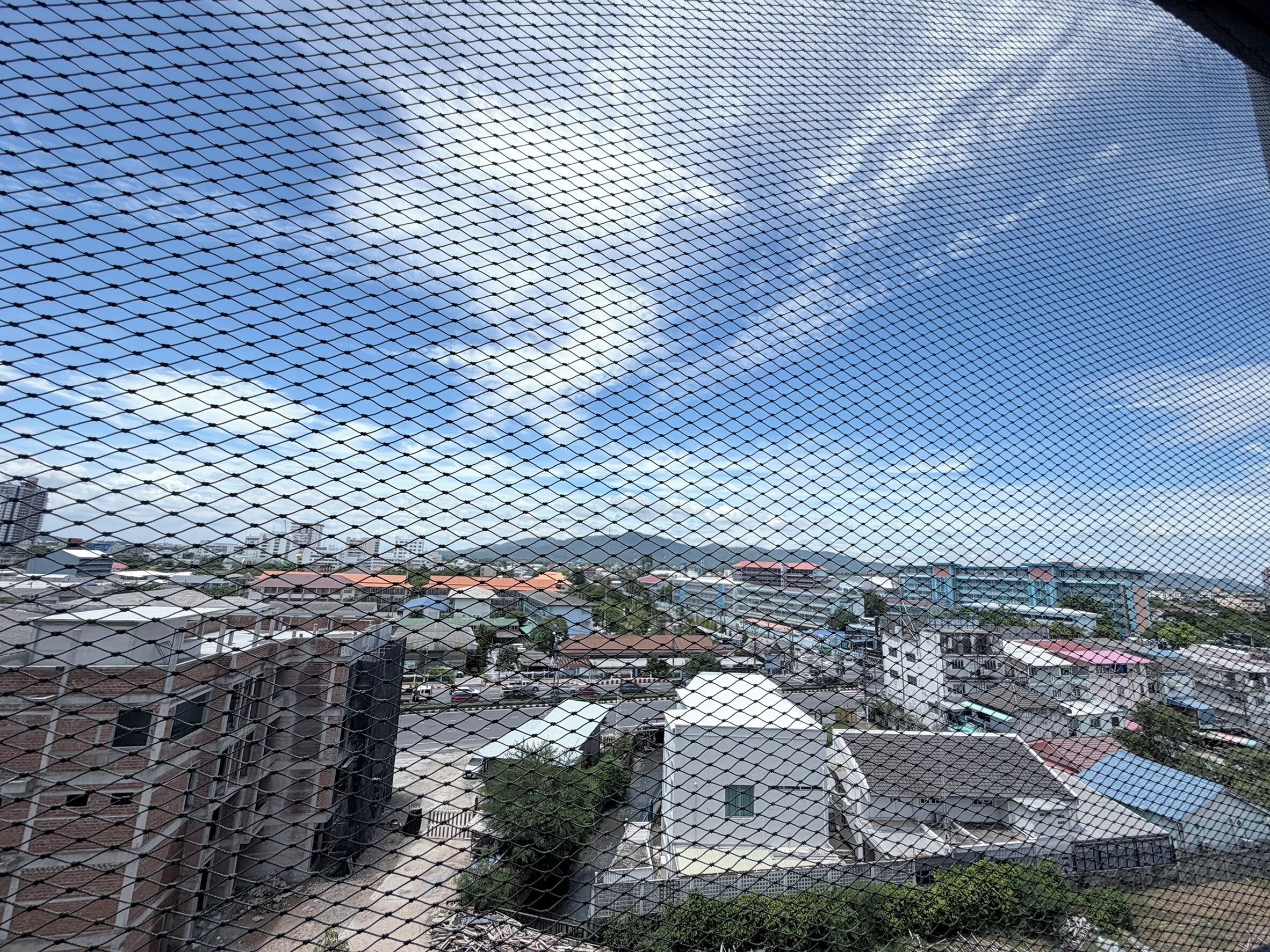 A cityscape with buildings, a clear sky, and a chain-link fence.