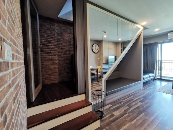 A modern interior with a brick wall, a wooden staircase, a dining area with a clock, and a large window. - Premire Luxe Hotel Chonburi (Chonburi)