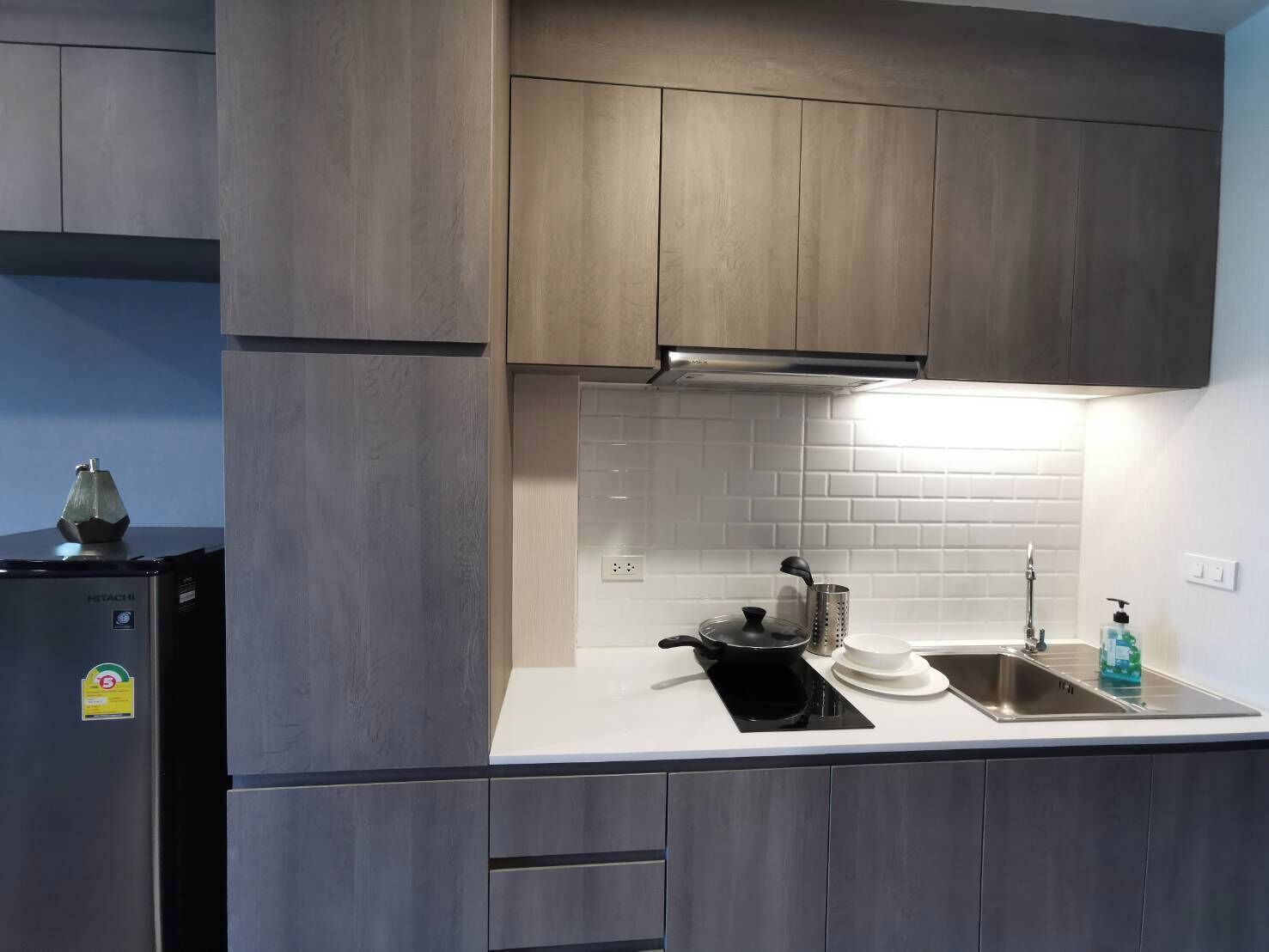 A modern kitchen with grey cabinets, a built-in stove, a sink, and a white tiled backsplash.