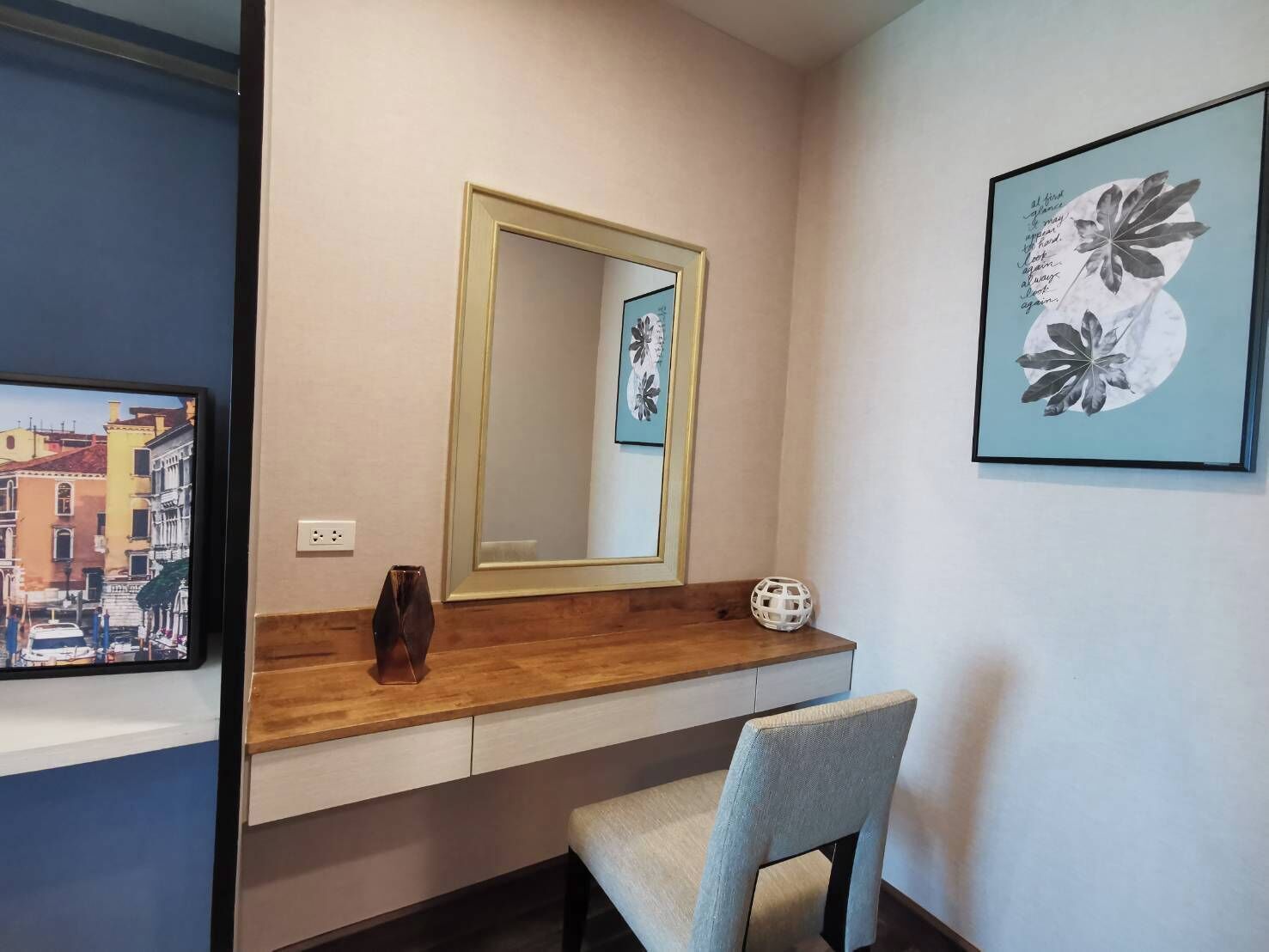 Una habitación con un tocador de madera, un espejo, una silla y dos obras de arte enmarcadas en la pared.