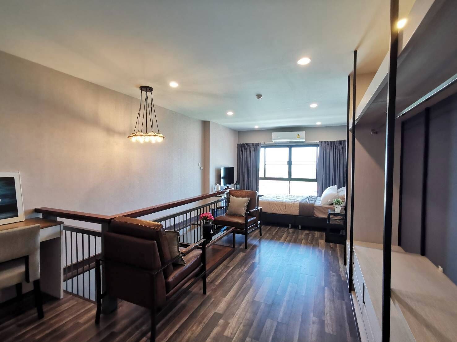 A modern hotel room with a wooden floor, a sofa, a bed, a desk, and a TV.