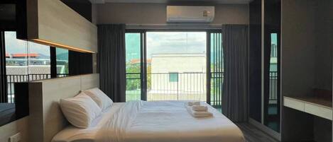 A modern hotel room with a large bed, a desk, and a balcony with a view.