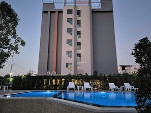 A swimming pool with lounge chairs, a tall building with multiple windows, and a hedge in the foreground. - Premire Luxe Hotel Chonburi (Chonburi)