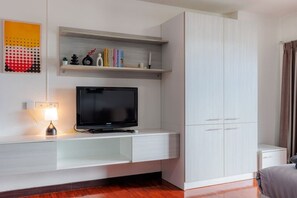 Une chambre moderne avec un téléviseur posé sur une console blanche, une petite étagère avec des livres et des objets décoratifs, et une grande armoire.