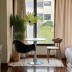 A room with a round table, two chairs, a potted plant, a bed, and a window with curtains. - Mid century style near Nimman and Maya (Tambon Chang Phueak)