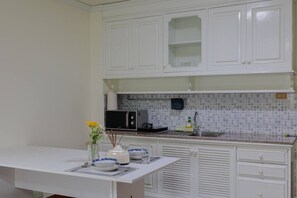 A kitchen with white cabinets, a microwave, a sink, and a dining table with a vase and plates. - Mid century style near Nimman and Maya (Tambon Chang Phueak)