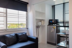 Une chambre moderne avec un canapé en cuir noir, une petite kitchenette équipée d’un four à micro-ondes et d’un grille-pain, et une fenêtre avec des stores.