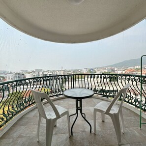 Ein Balkon mit rundem Tisch und zwei Stühlen, Blick auf eine Stadtansicht, und einem Metallgeländer.