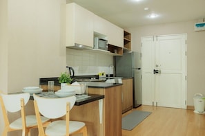 A compact kitchen with a refrigerator, microwave, and a small sink. There are two chairs and a dining table with plates and glasses. - Stay Classy – Pool• Gym• Balcony (Chiang Mai)