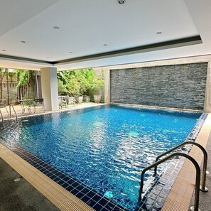 A swimming pool with a tiled edge, a metal handrail, and a stone wall in the background. - Stay Classy – Pool• Gym• Balcony (Chiang Mai)