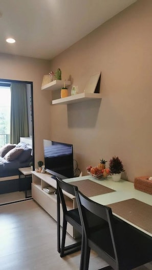 Ett modernt sovrum med en säng, en tv, ett skrivbord och en stol. Det finns hyllor med dekorativa föremål och ett fönster med gardiner.