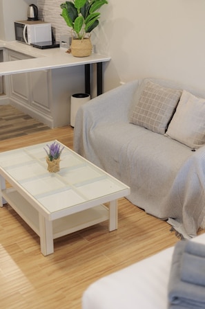 Ein modernes Wohnzimmer mit einem weißen Couchtisch, einer Couch und einer Küchenzeile mit einer Mikrowelle und einer Topfpflanze.