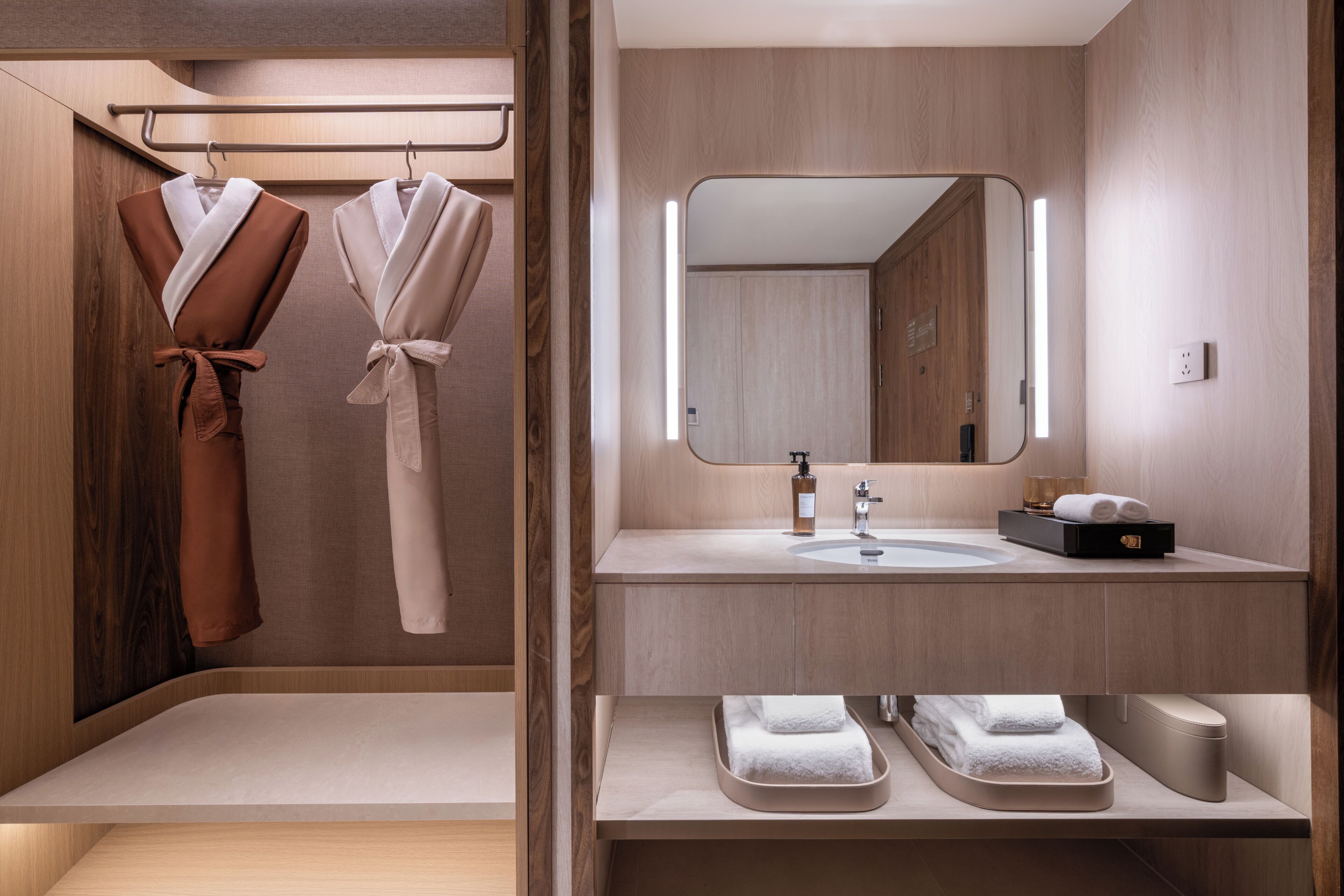 A modern bathroom with wooden paneling, a large mirror, a sink with toiletries, and two towels on a shelf.