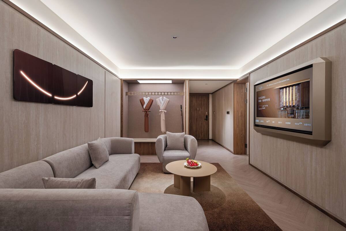 A modern living room with a sofa, armchair, coffee table, and a flat-screen TV mounted on the wall.