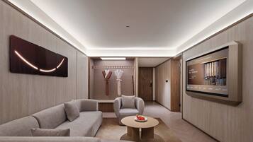 A modern living room with a sofa, armchair, coffee table, and a flat-screen TV mounted on the wall.