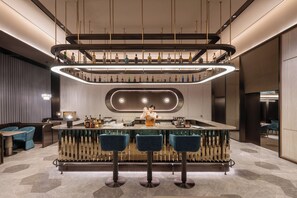 Zona de bar moderna con una barra central, tres taburetes y un camarero.