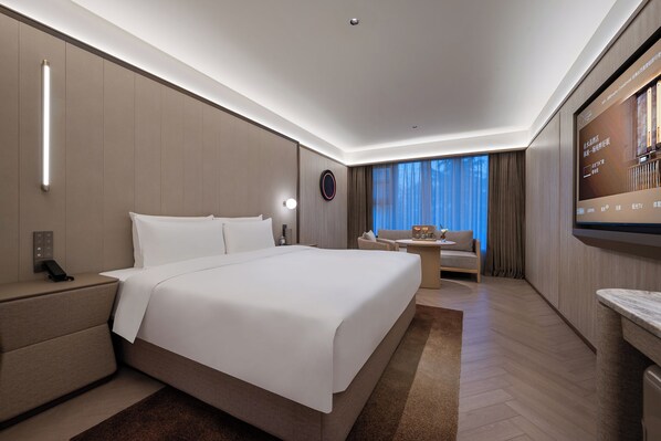 A modern hotel room with a large bed, bedside table, and a flat-screen TV mounted on the wall.