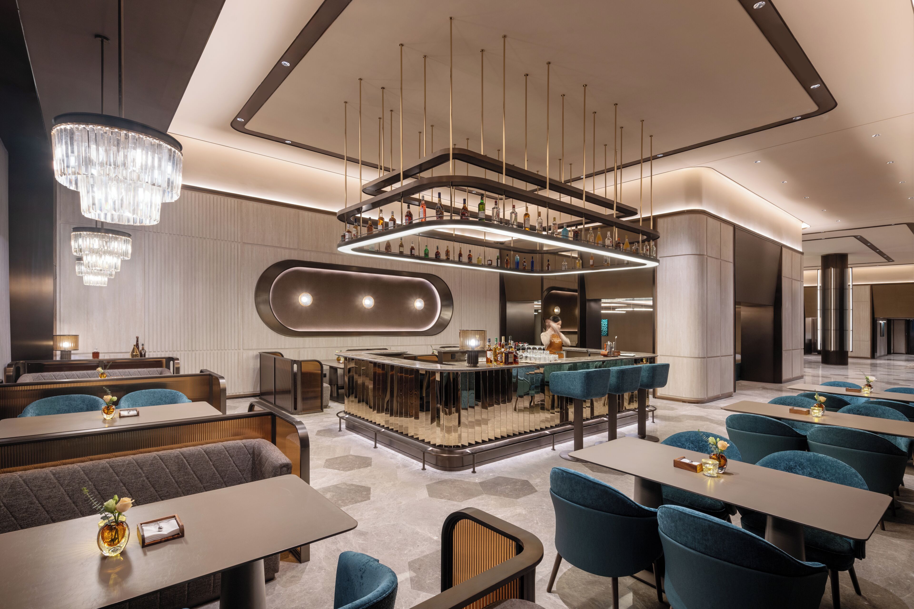 A modern hotel lobby with a bar area, seating arrangements, and a chandelier.
