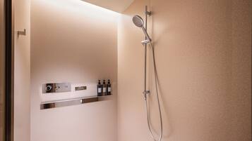 Ducha con cabezal de ducha de mano y grifo empotrado, panel de control con botones y pequeño estante con botellas.