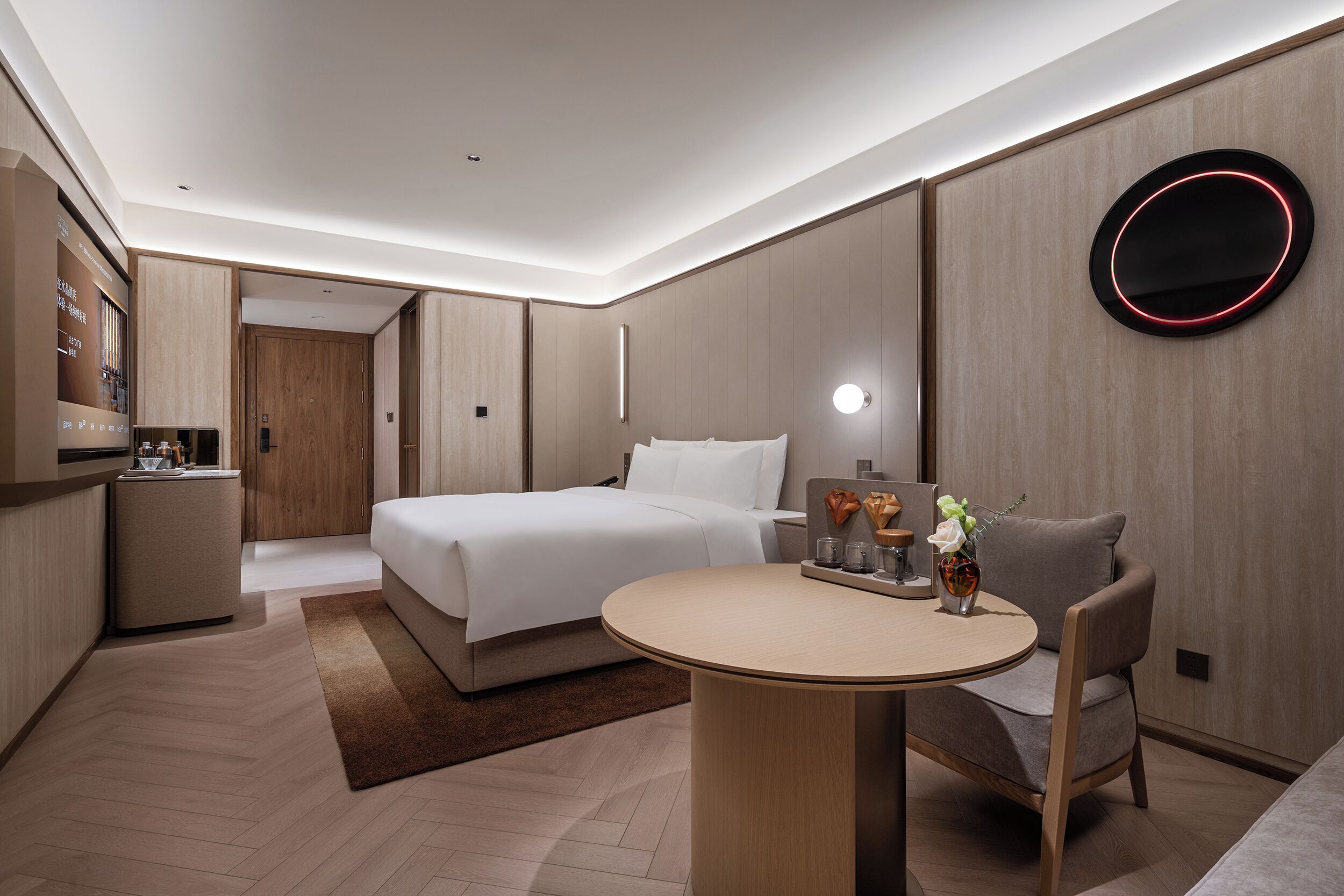 Una habitación de hotel moderna con cama, mesita de noche, silla y una mesa redonda con un florero.
