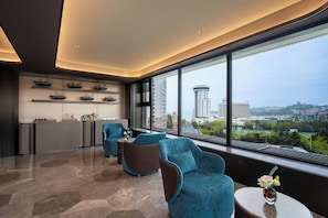 A modern hotel room with a large window, a kitchen area, and seating with a view.