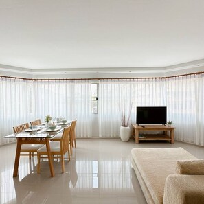 A modern living room with a dining area, a flat-screen TV, and a large window with sheer curtains. - Big and Brightroom in Nimman (Suthep)