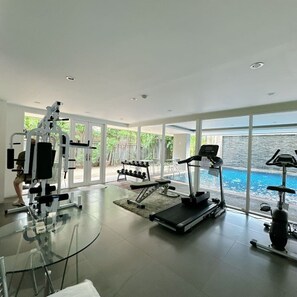 A modern gym with exercise equipment, a treadmill, and a view of a swimming pool. - Stay Calm – Pool• Gym• Balcony (Suthep)