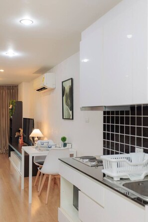 A modern kitchen with white cabinetry, a dining area with a table and chairs, and a black tiled backsplash. - Stay Calm – Pool• Gym• Balcony (Suthep)