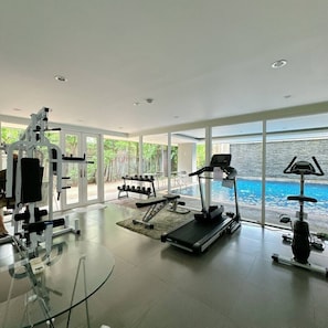 Ein modernes Fitnessstudio mit Trainingsgeräten, einem Laufband und Blick auf einen Swimmingpool.