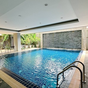 A swimming pool with a tiled edge, a metal handrail, and a stone wall backdrop. - Spacious Studio with Balcony in Nimman Soi 15 | Pool, Gym & Washer (Chiang Mai)