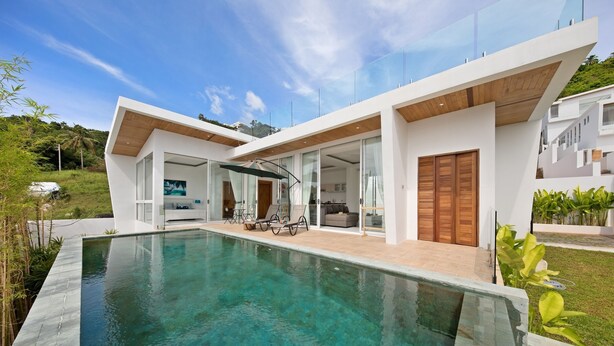 Een modern huis met een zwembad, glazen deuren en een houten terras.