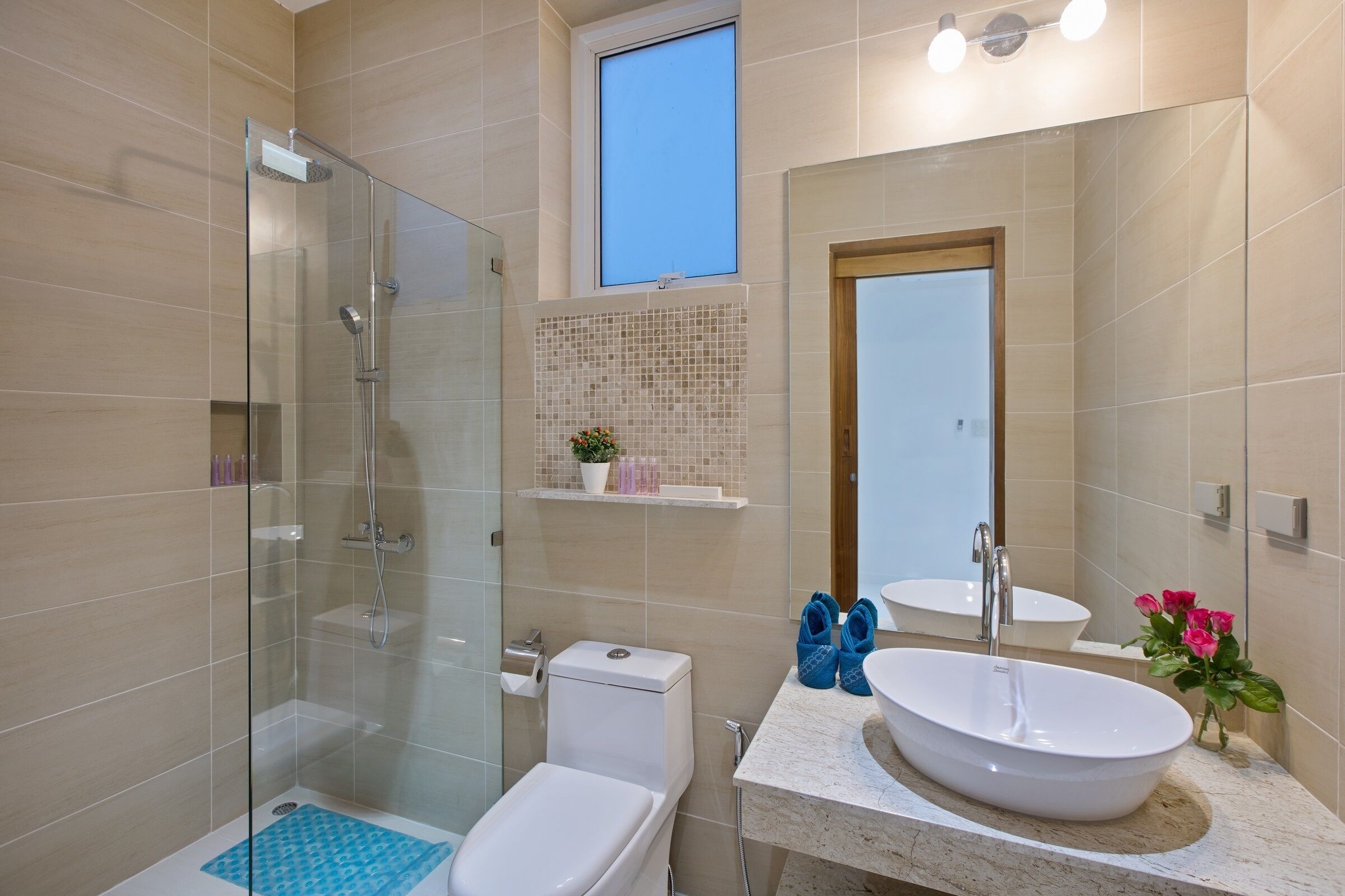 Un baño moderno con ducha envuelta en vidrio, un inodoro blanco, un lavabo con una gran pila y un espejo sobre el lavabo.