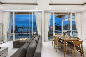 Ein modernes Wohnzimmer mit einer Couch, einem Esstisch und Stühlen, große Glasüren, die auf einen Balkon mit Blick auf Palmen führen.