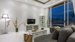 Een moderne woonkamer met een flatscreen televisie, witte meubels, een glazen kast en uitzicht op het groen.